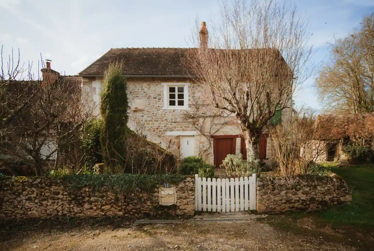 Maison de campagne en pierre avec jardin clos derrière un muret et un portillon blanc