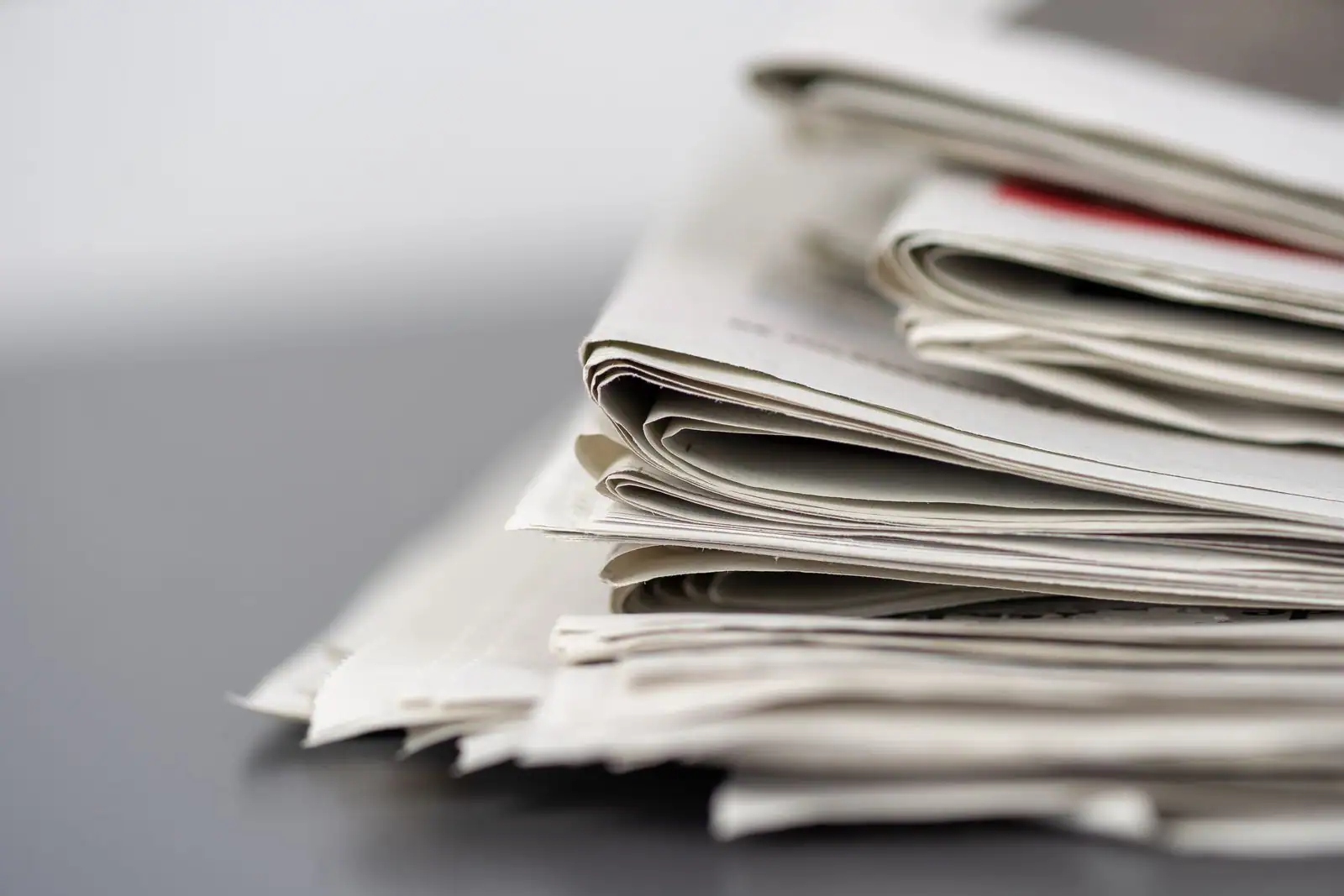 Une pile de journaux papier pliés posée sur une surface claire, illustrant le suivi de l'actualité.