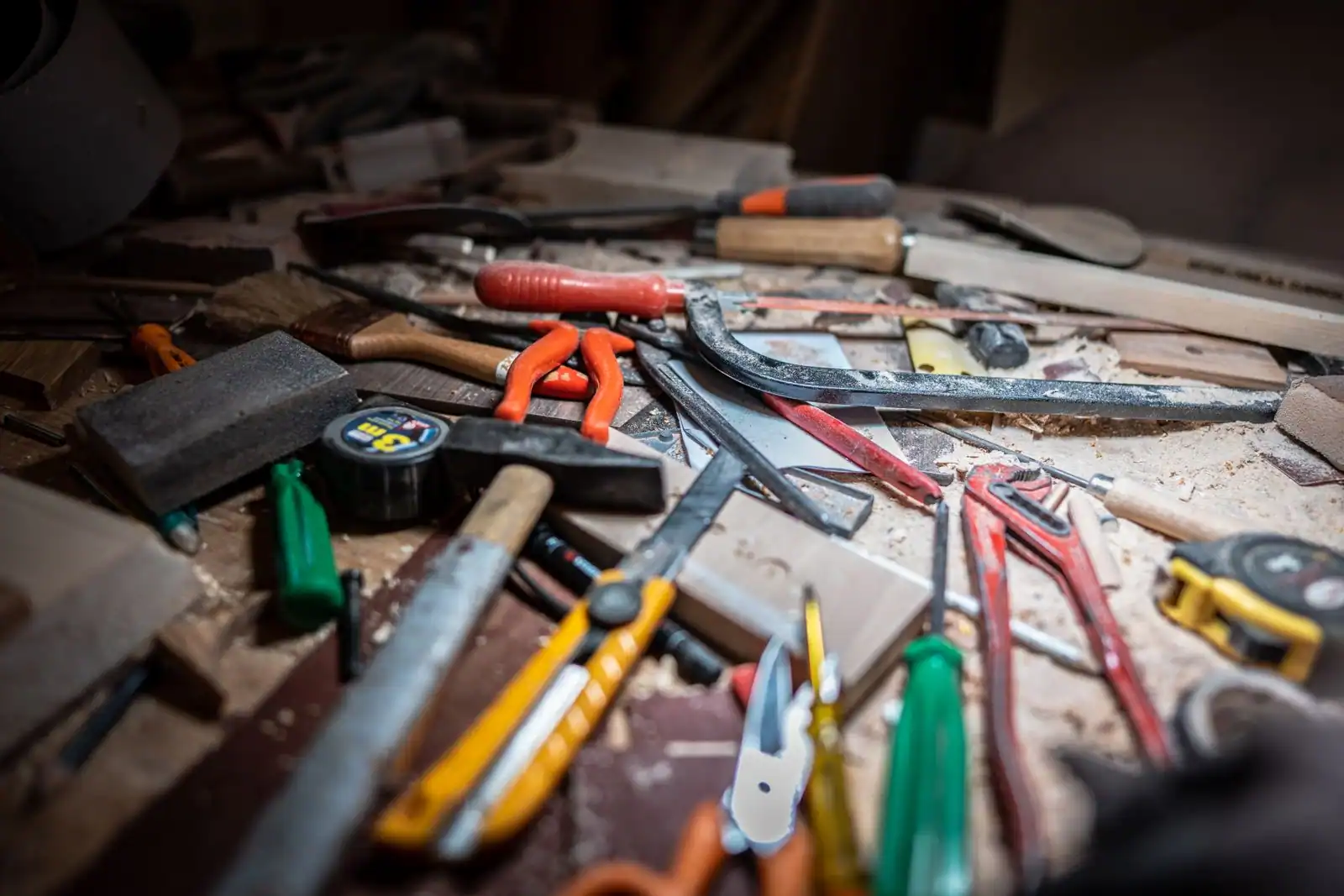 Établi d'atelier encombré de nombreux outils à main : scies, marteau, tournevis, ciseaux à bois et mètre ruban