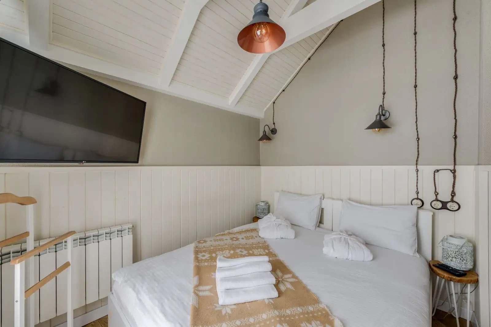 Chambre aux teintes douces et chaleureuses, lit blanc, plaid ocre et suspensions à lumière chaude.