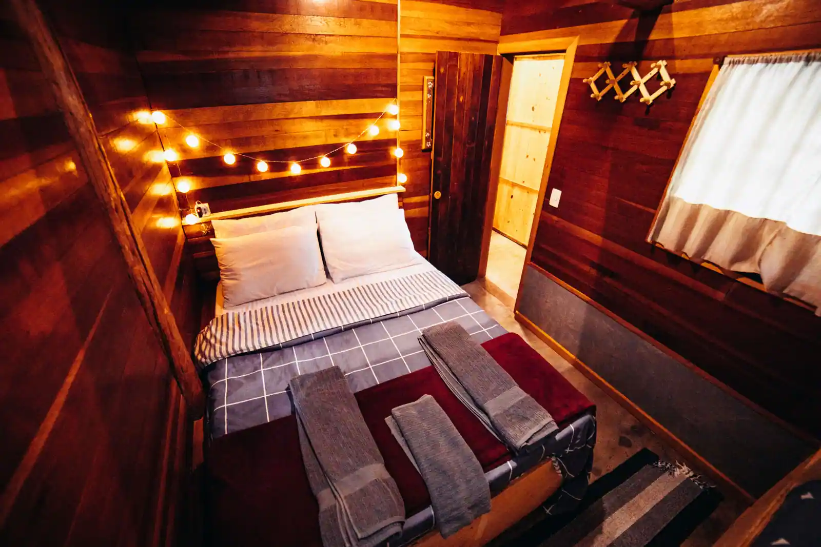 Chambre chaleureuse aux murs en bois, lit douillet et guirlande lumineuse à la lumière dorée.