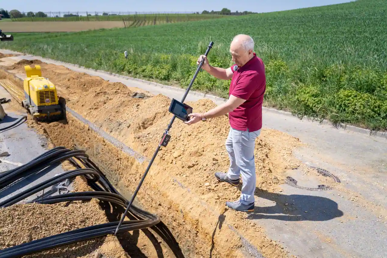 Pose de fourreaux dans une tranchée de chantier, un technicien contrôle le tracé du réseau enterré.