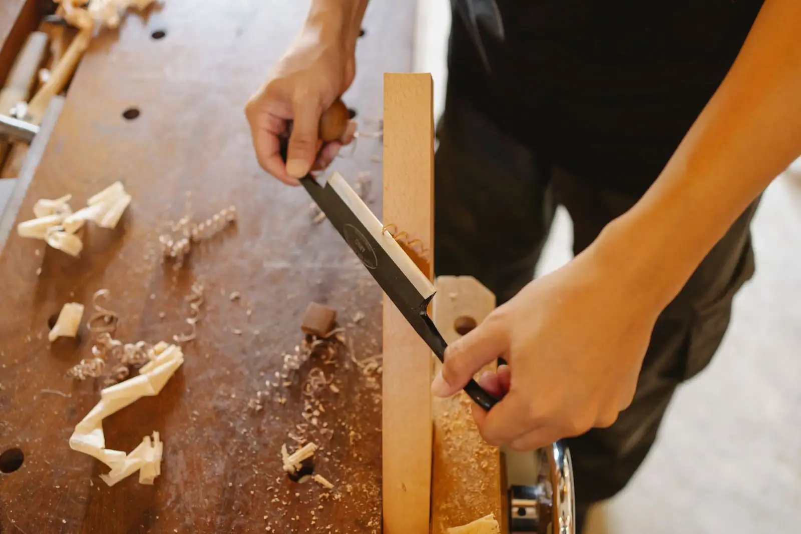 Mains d'un artisan menuisier façonnant une pièce de bois à l'établi, copeaux tout autour.