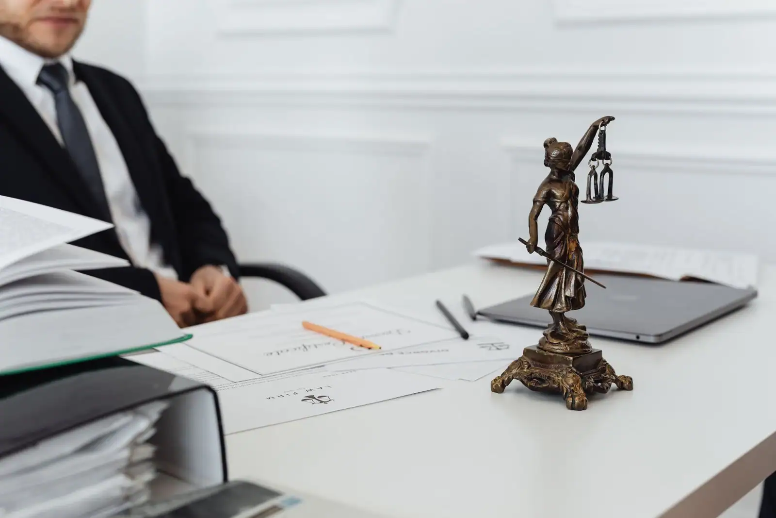 Statue de la justice tenant une balance sur le bureau d'un professionnel du droit, avec des documents juridiques.