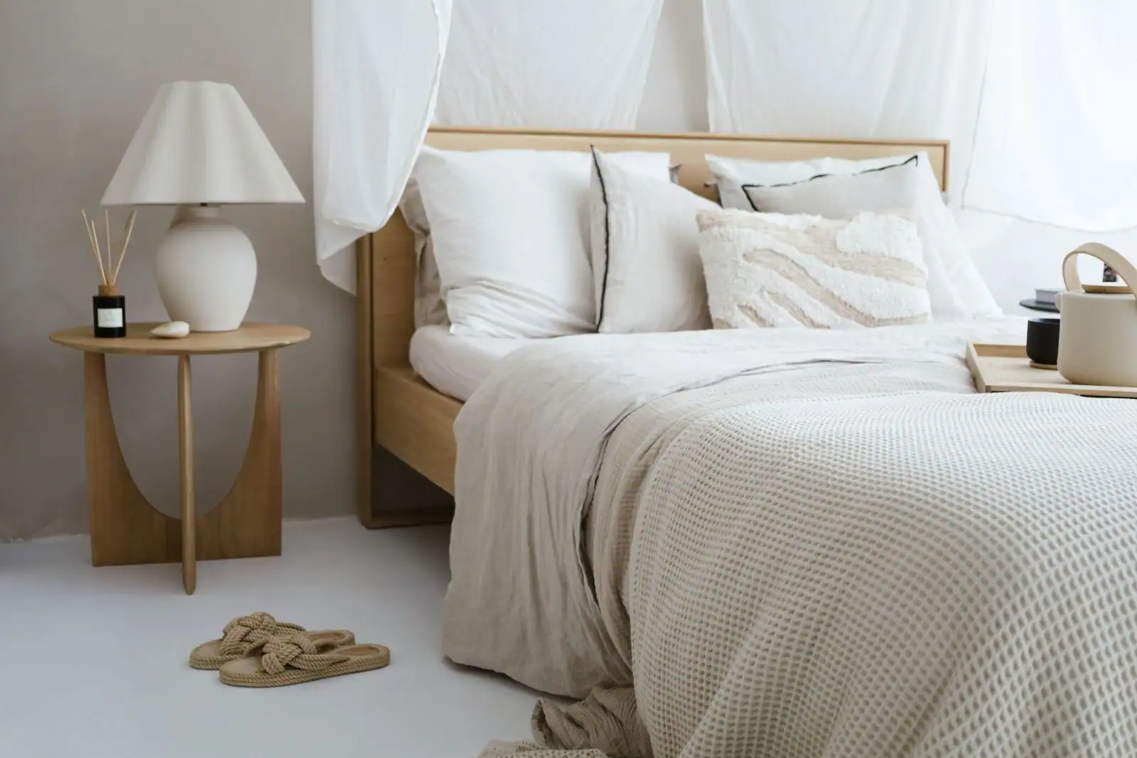 Chambre cosy aux tons neutres : lit en bois, linge de lit en lin superposé et lampe de chevet