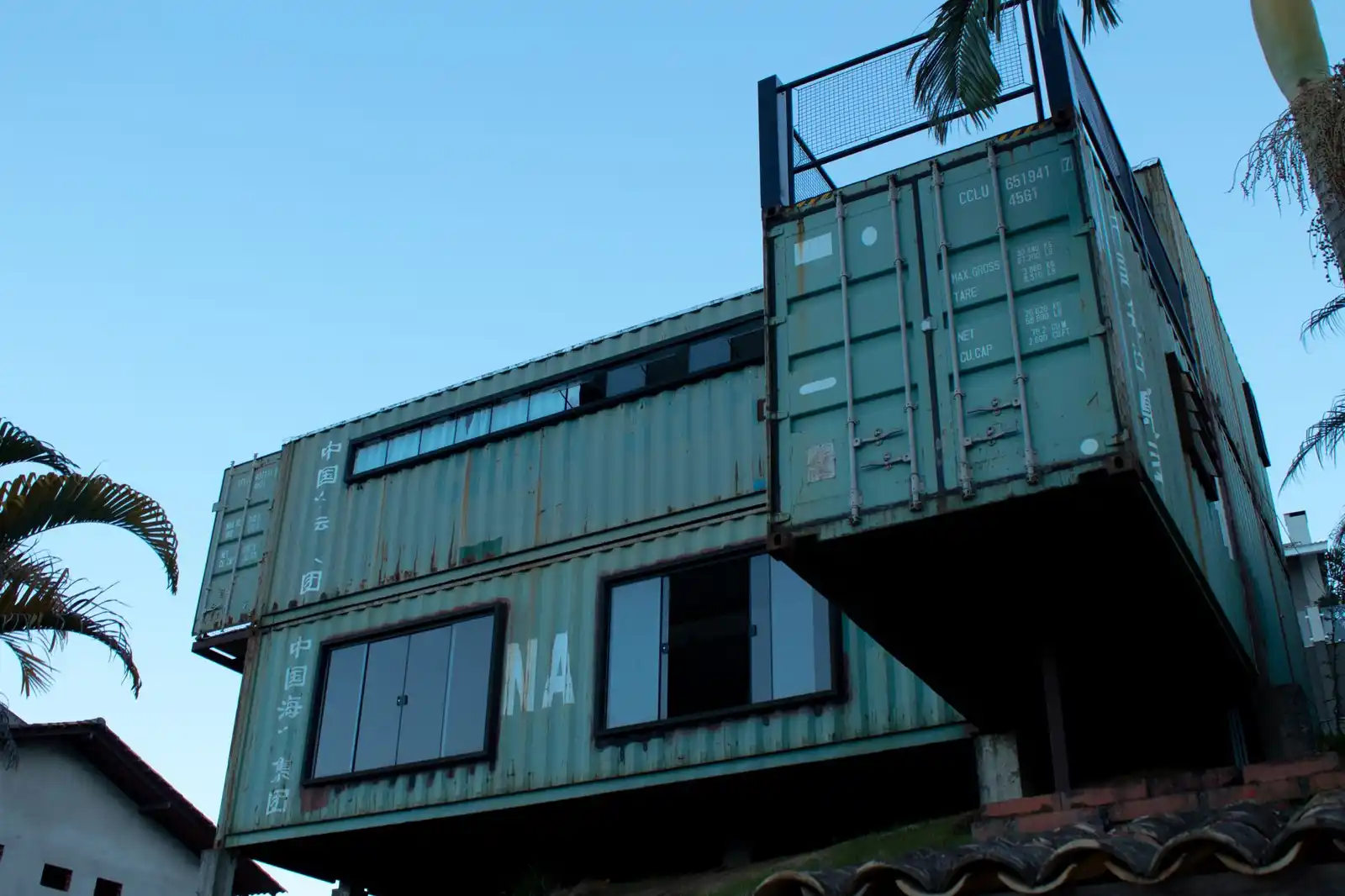 Maison individuelle construite à partir de conteneurs maritimes empilés, fenêtres découpées dans l'acier.