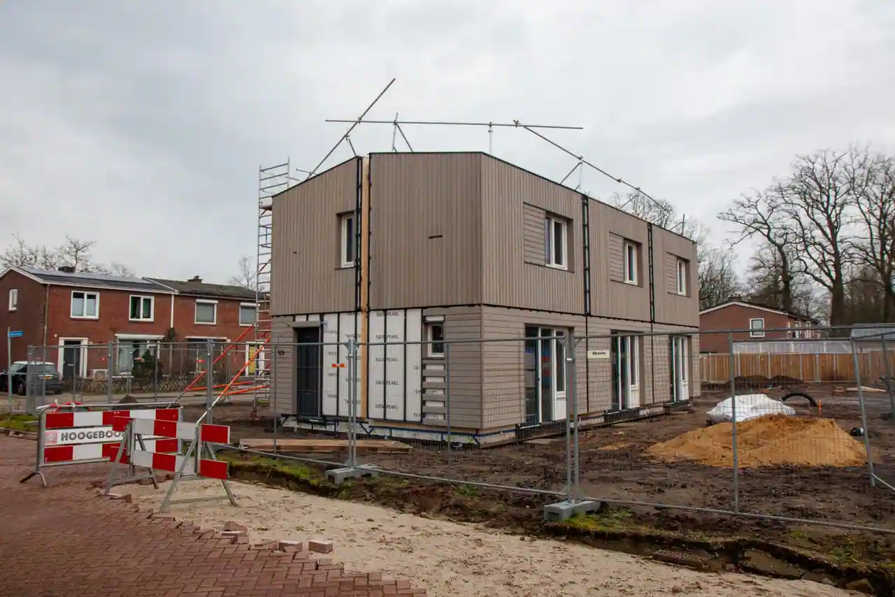 Une maison individuelle en cours de construction, entourée d'échafaudages et de barrières de chantier, par temps couvert.