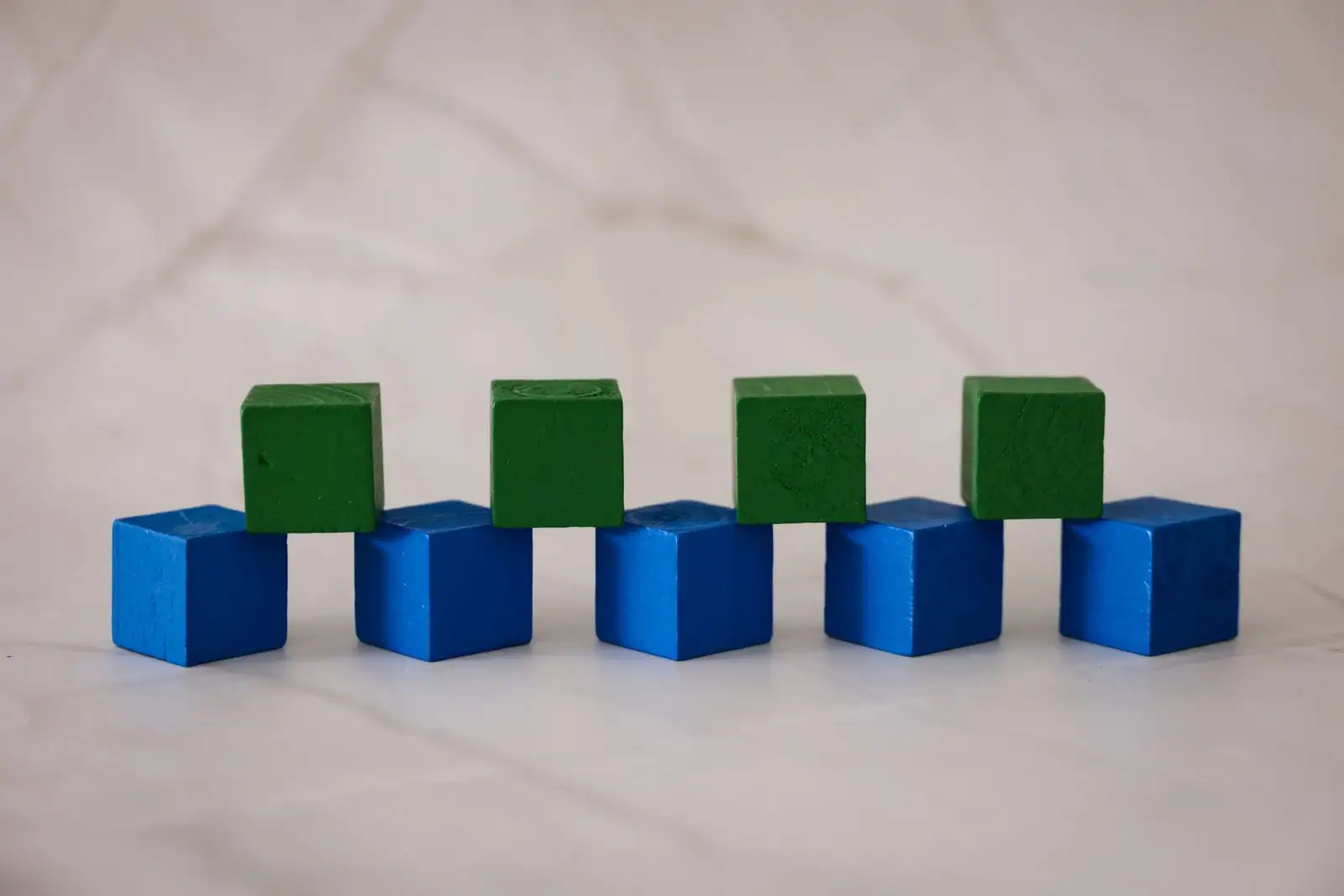 Cubes en bois bleus et verts disposés en blocs, évoquant un jeu de construction par cubes