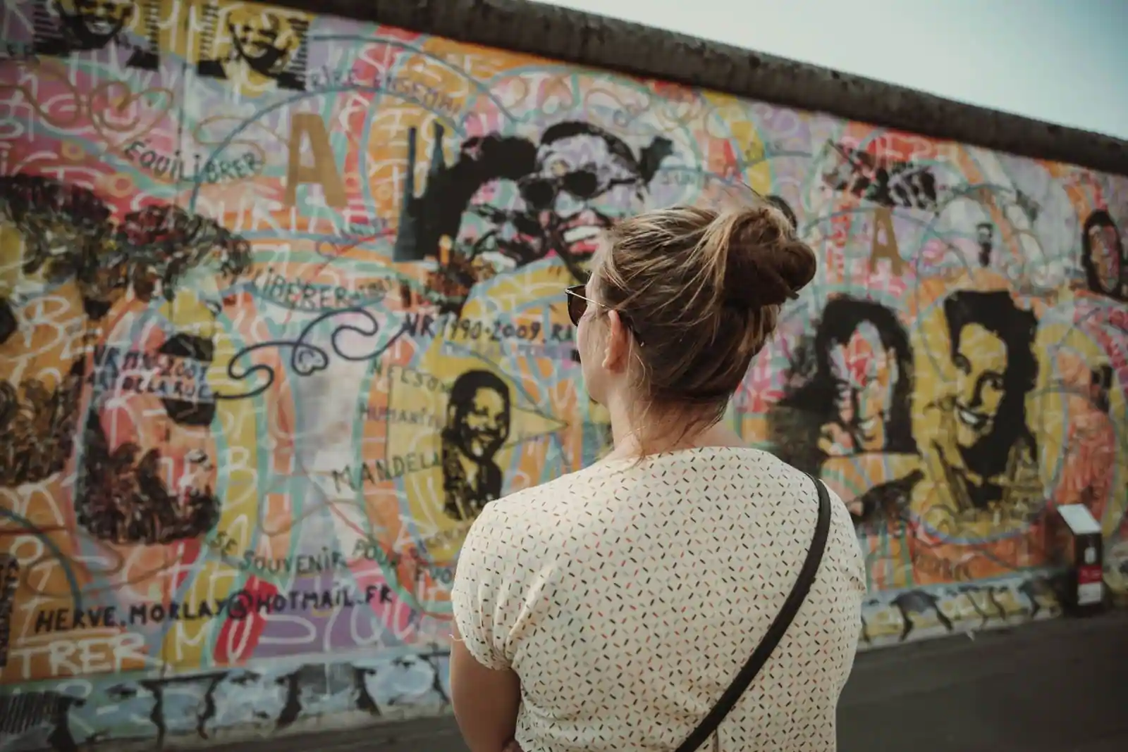 Femme de dos observant une section peinte du mur de Berlin couverte de fresques colorées (East Side Gallery)
