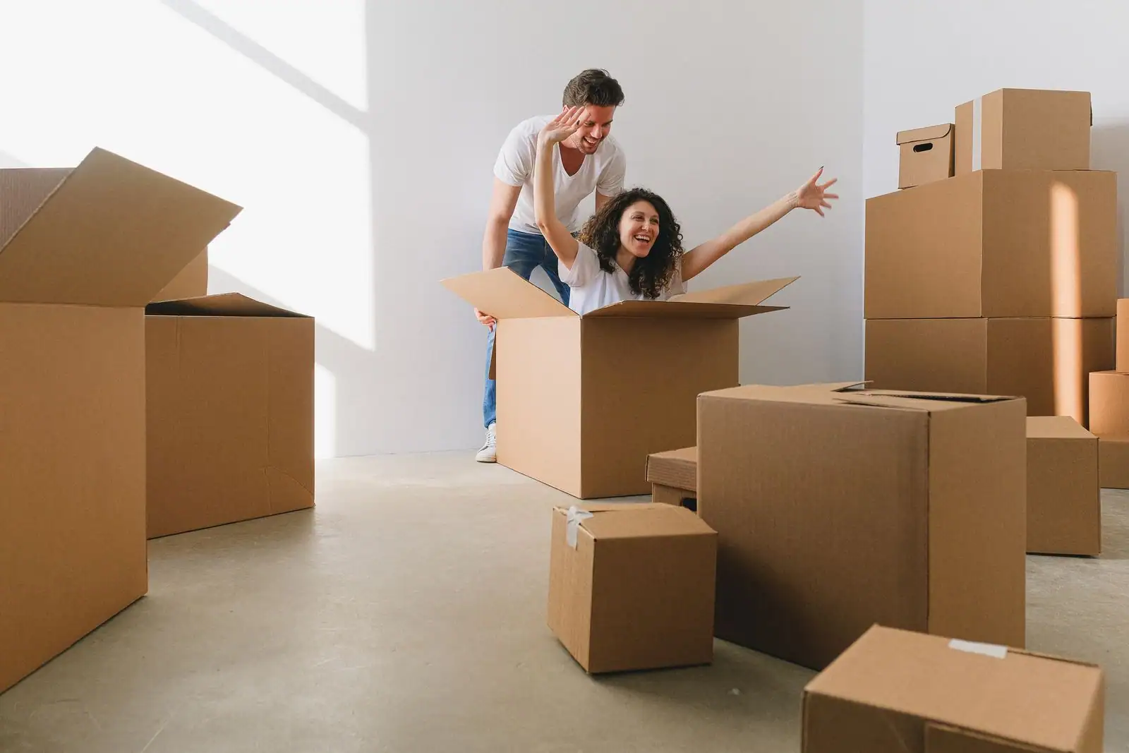 Couple souriant entouré de cartons de déménagement dans une pièce lumineuse d'une nouvelle maison