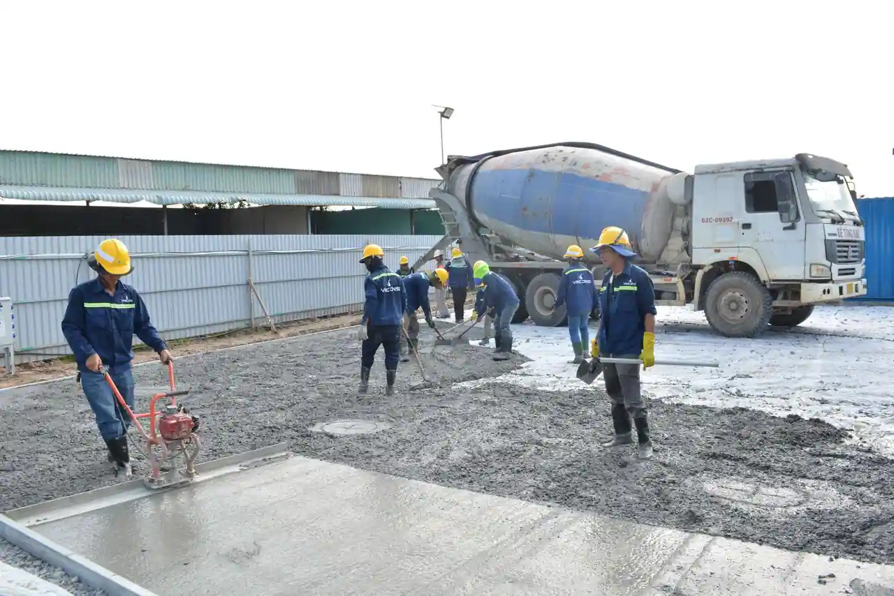 Des ouvriers coulent et nivellent une dalle de béton frais sur un chantier, devant un camion toupie.