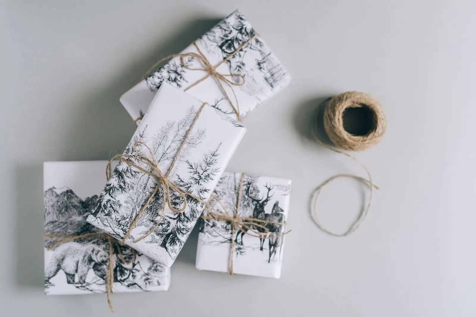 Cadeaux emballés à la main dans du papier imprimé et noués de ficelle, à côté d'une bobine de ficelle.