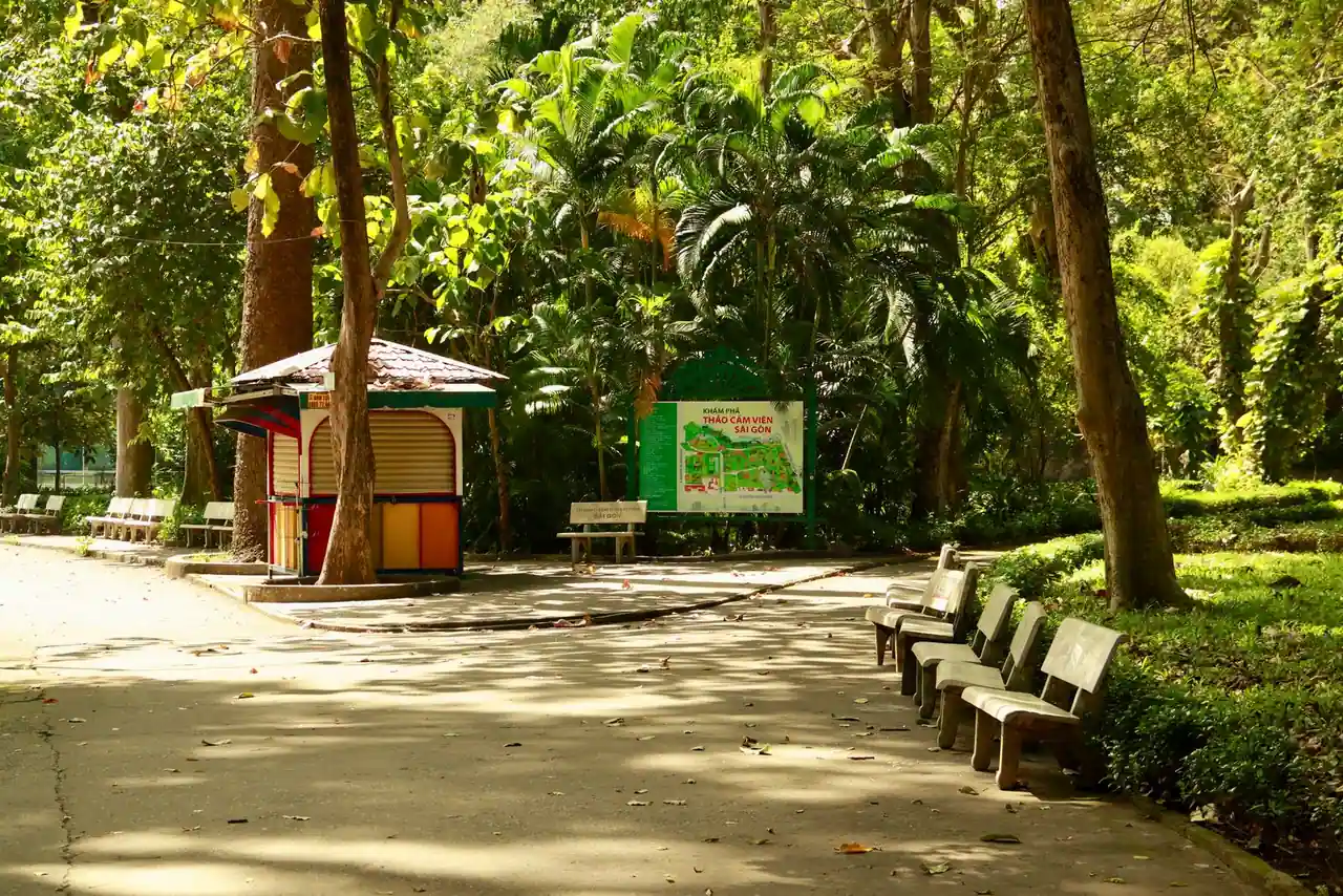 Allée ombragée d'un parc arboré avec des bancs et une végétation dense le long du chemin