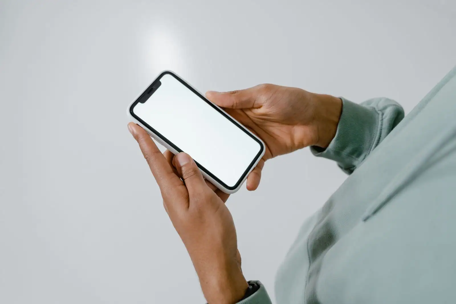 Personne tenant à deux mains un smartphone à l'écran blanc, sur le thème de la location de téléphone