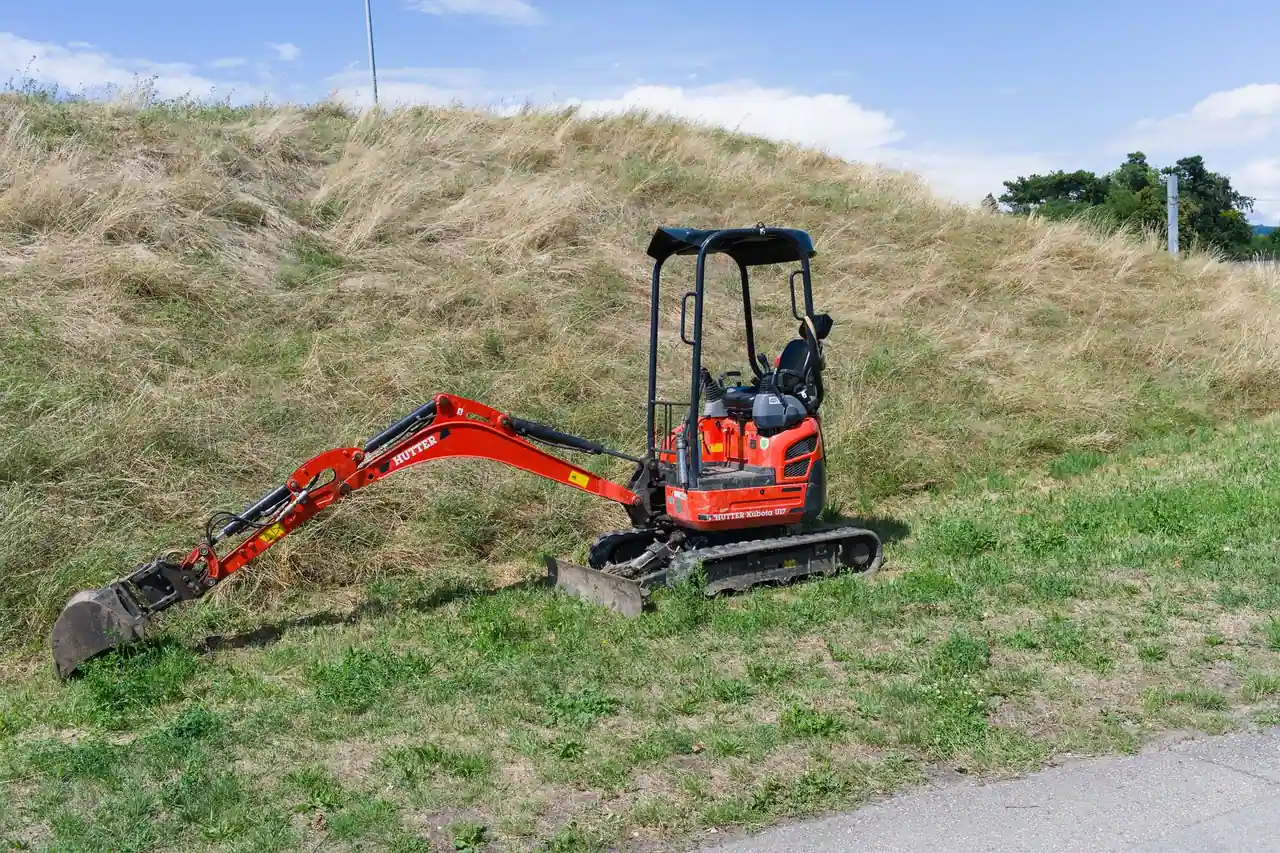 Mini-pelle compacte sur chenilles, équipée d'un godet, stationnée sur un talus herbeux ensoleillé
