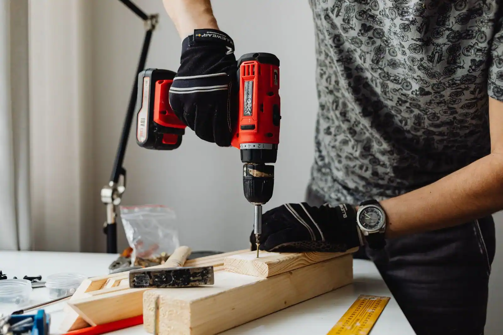 Perceuse-visseuse sans fil rouge utilisée pour percer une planche de bois, mains gantées