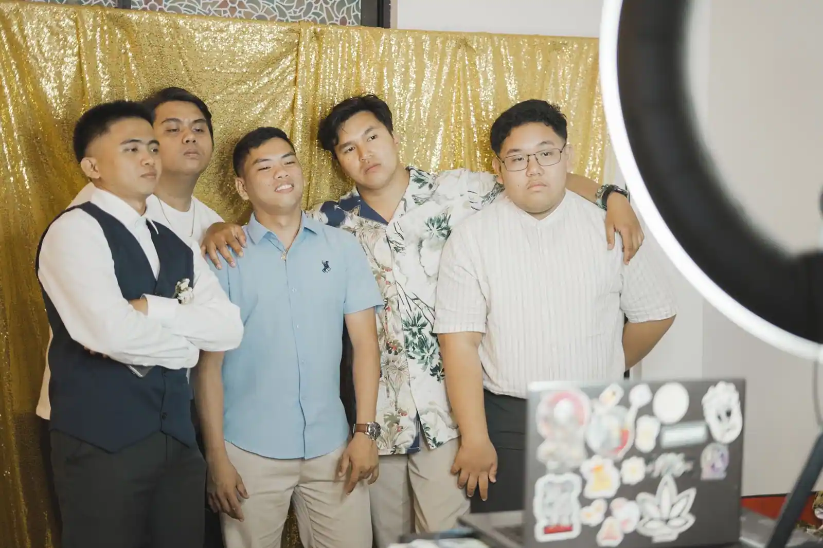 Des invités prennent la pose devant un fond doré de photobooth, éclairés par une ring light.