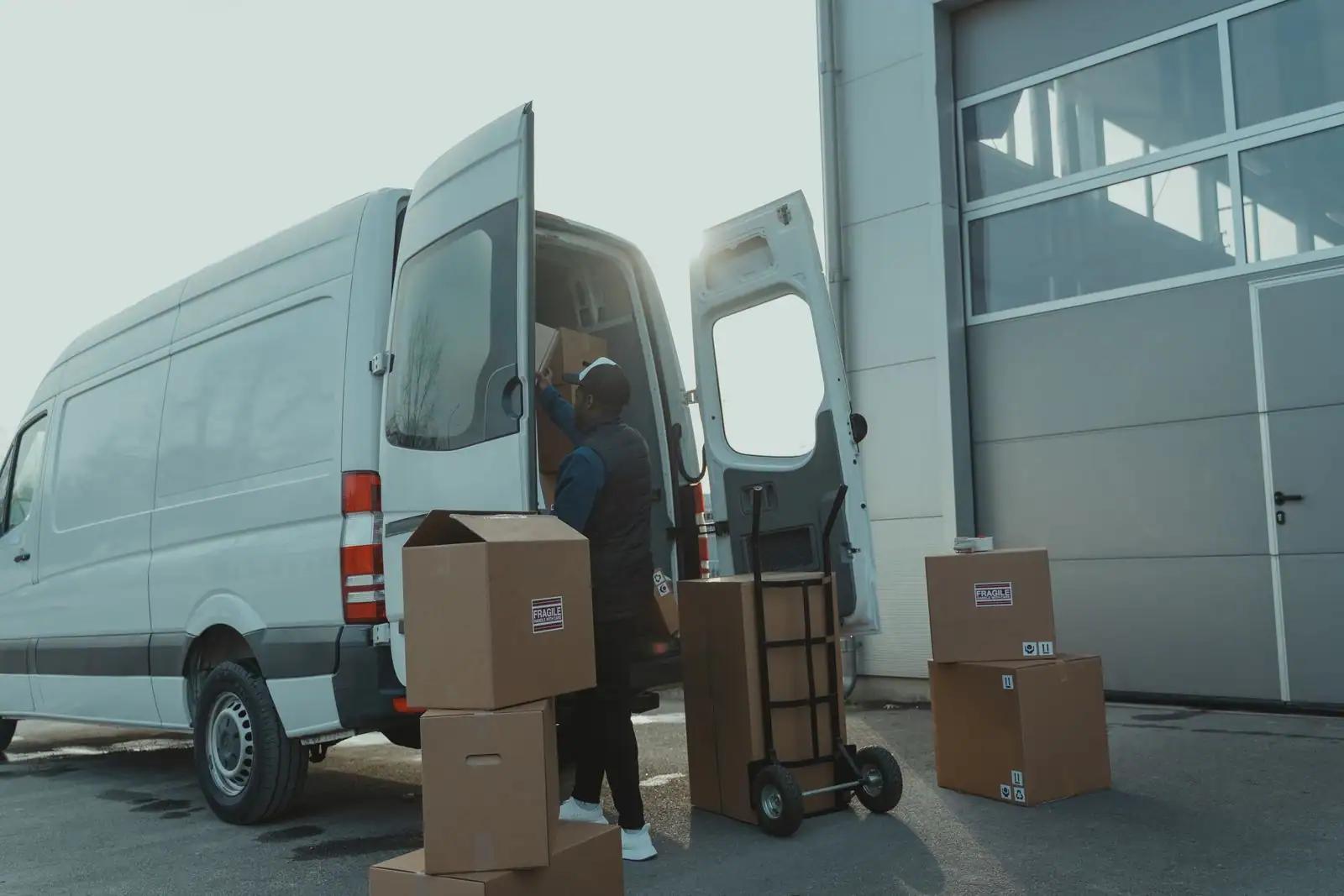 Fourgon utilitaire blanc aux portes arrière ouvertes, devant lequel une personne charge des cartons