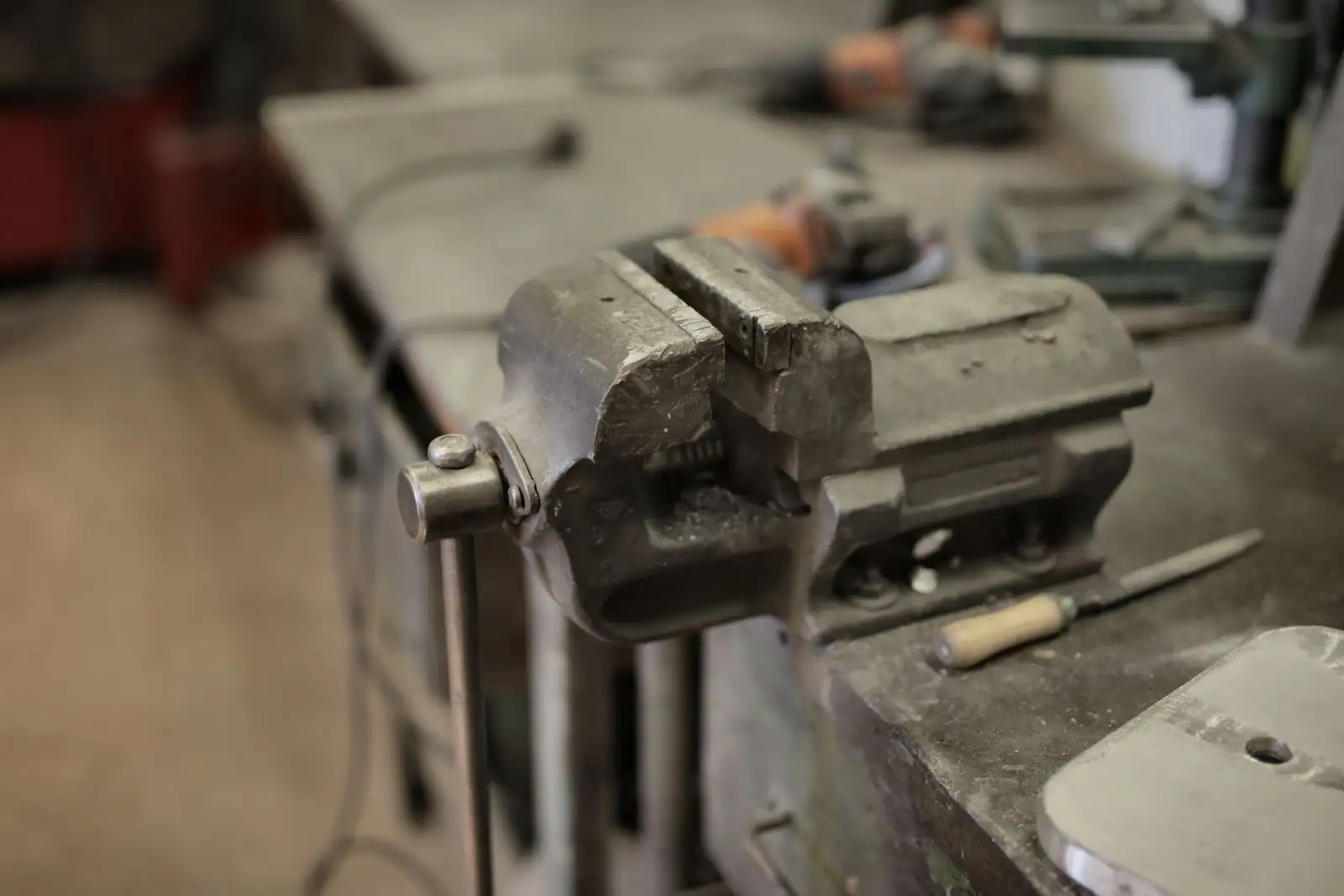 Un étau métallique fixé sur un établi dans un atelier, avec des outils posés en arrière-plan