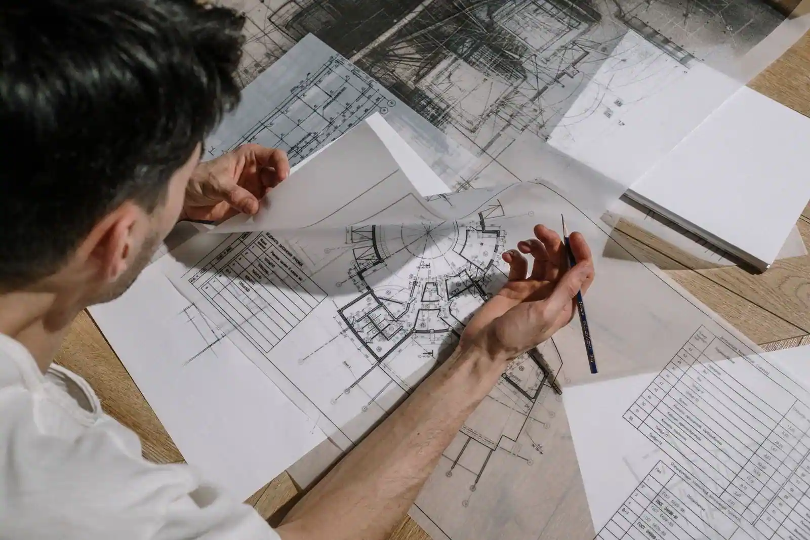 Une personne examine des plans d'architecte de maison, un crayon à la main, sur une table de travail