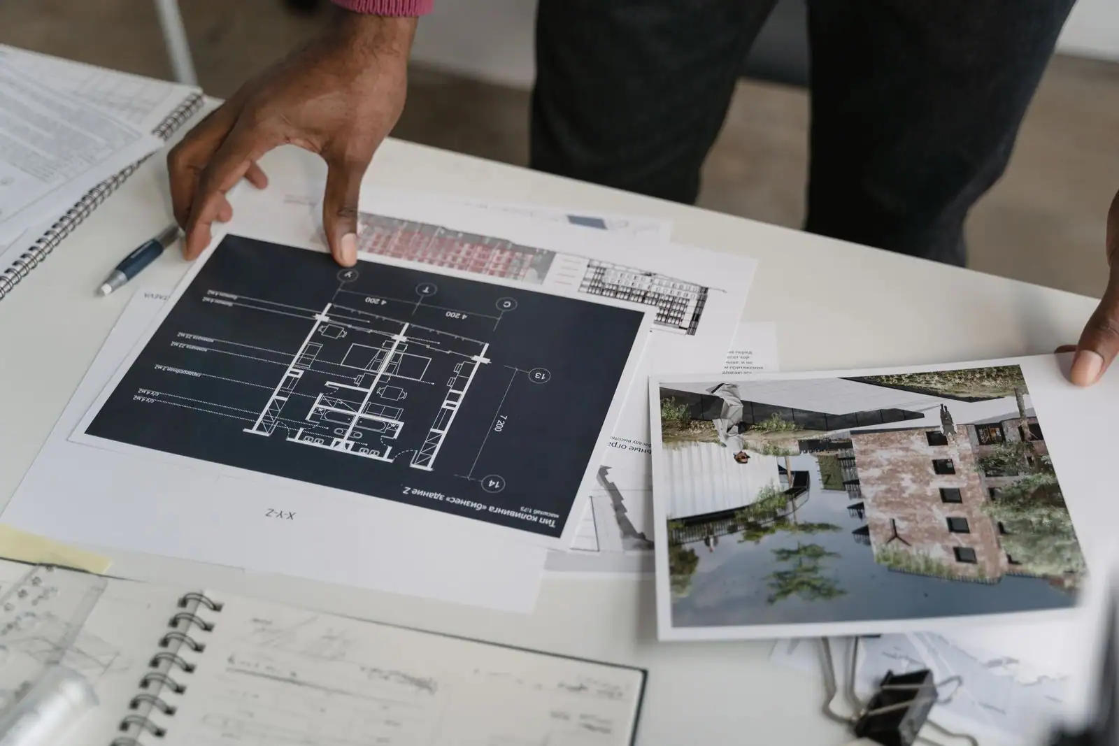 Des plans d'architecte et le rendu d'un bâtiment étalés sur une table de travail.