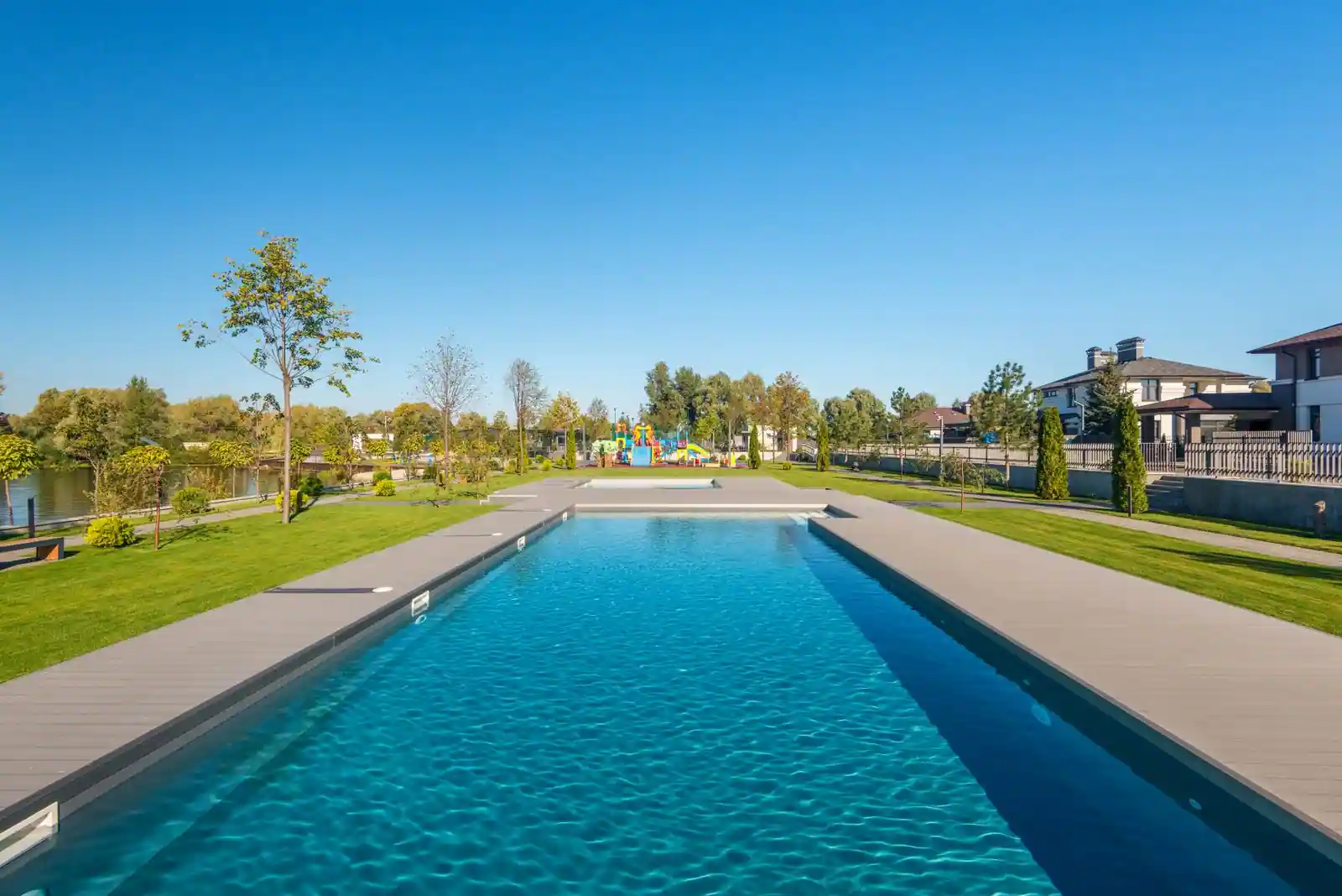 Grande piscine extérieure enterrée rectangulaire avec terrasse en bois composite et pelouse paysagée