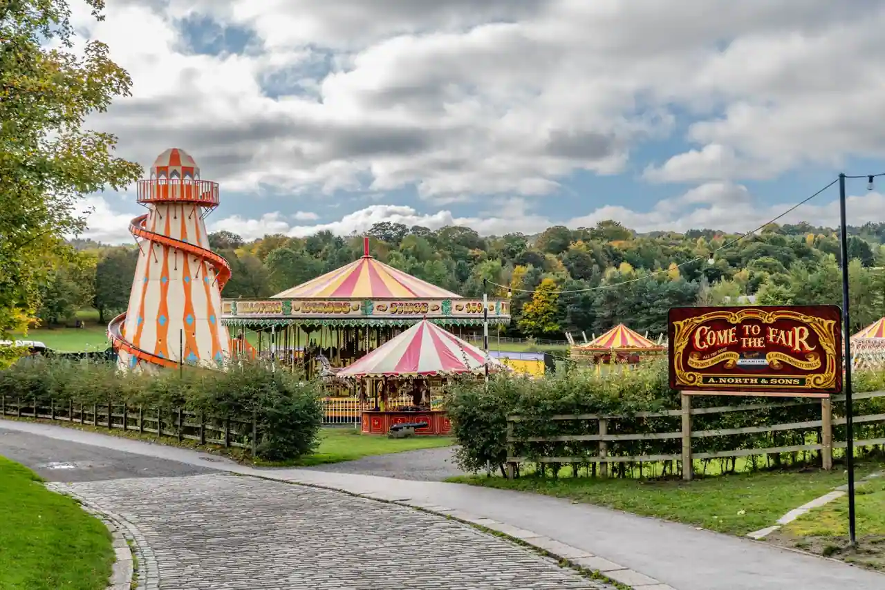 Allée d'un parc d'attractions familial bordée d'arbres avec un manège en arrière-plan