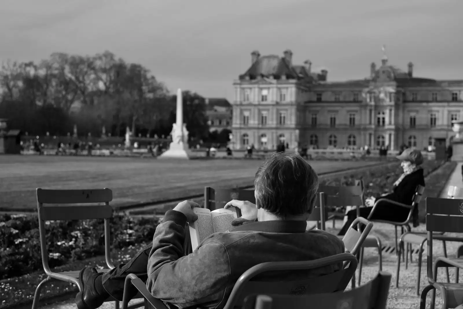 Vue du palais du Luxembourg depuis le jardin, avec des chaises et une personne en train de lire au premier plan.