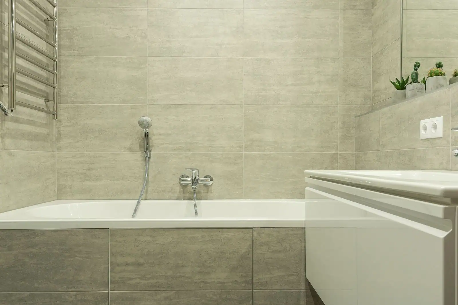 Salle de bain carrelée beige avec baignoire, mitigeur mural et meuble vasque blanc