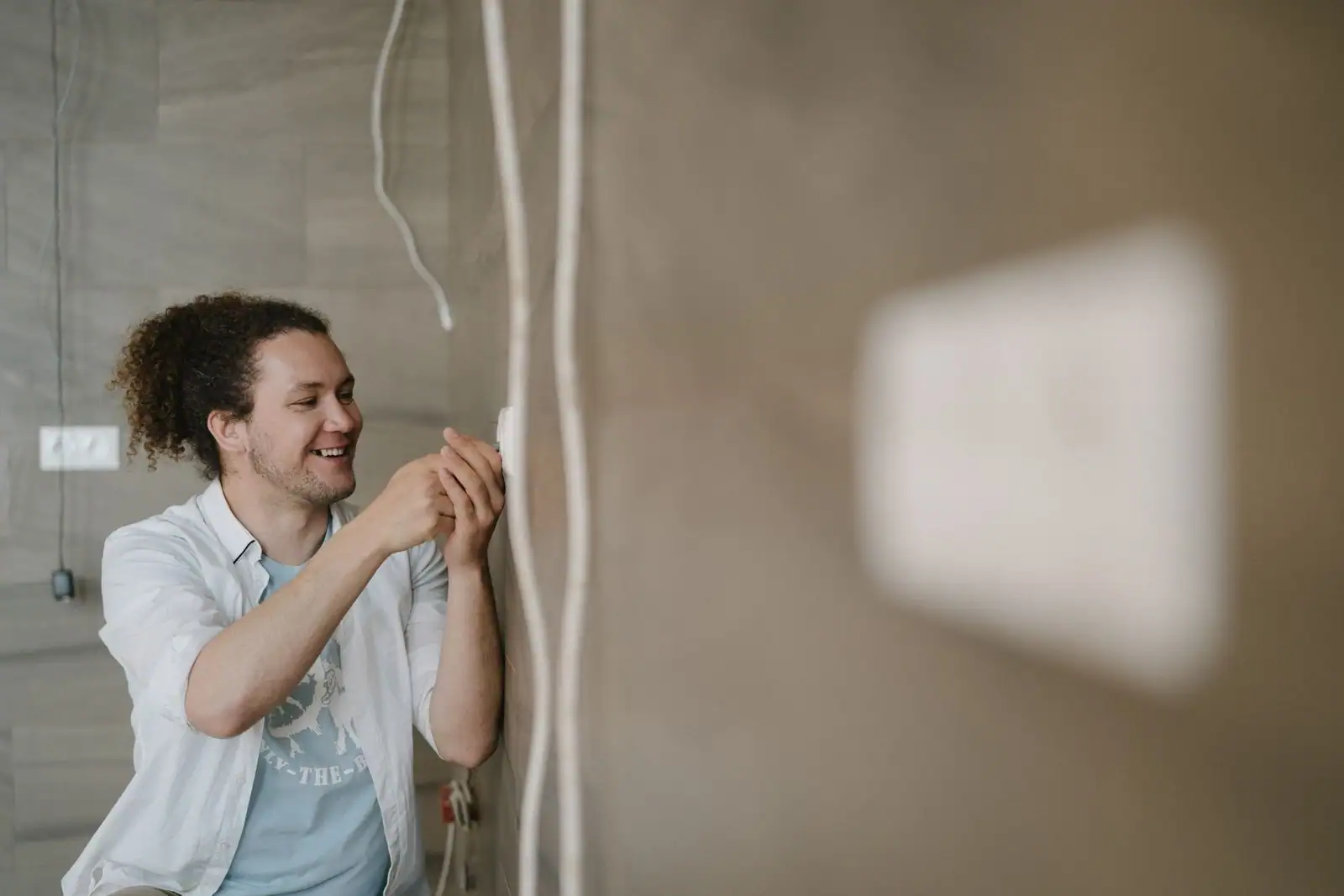 Professionnel souriant intervenant sur une prise électrique murale à l'intérieur d'un logement