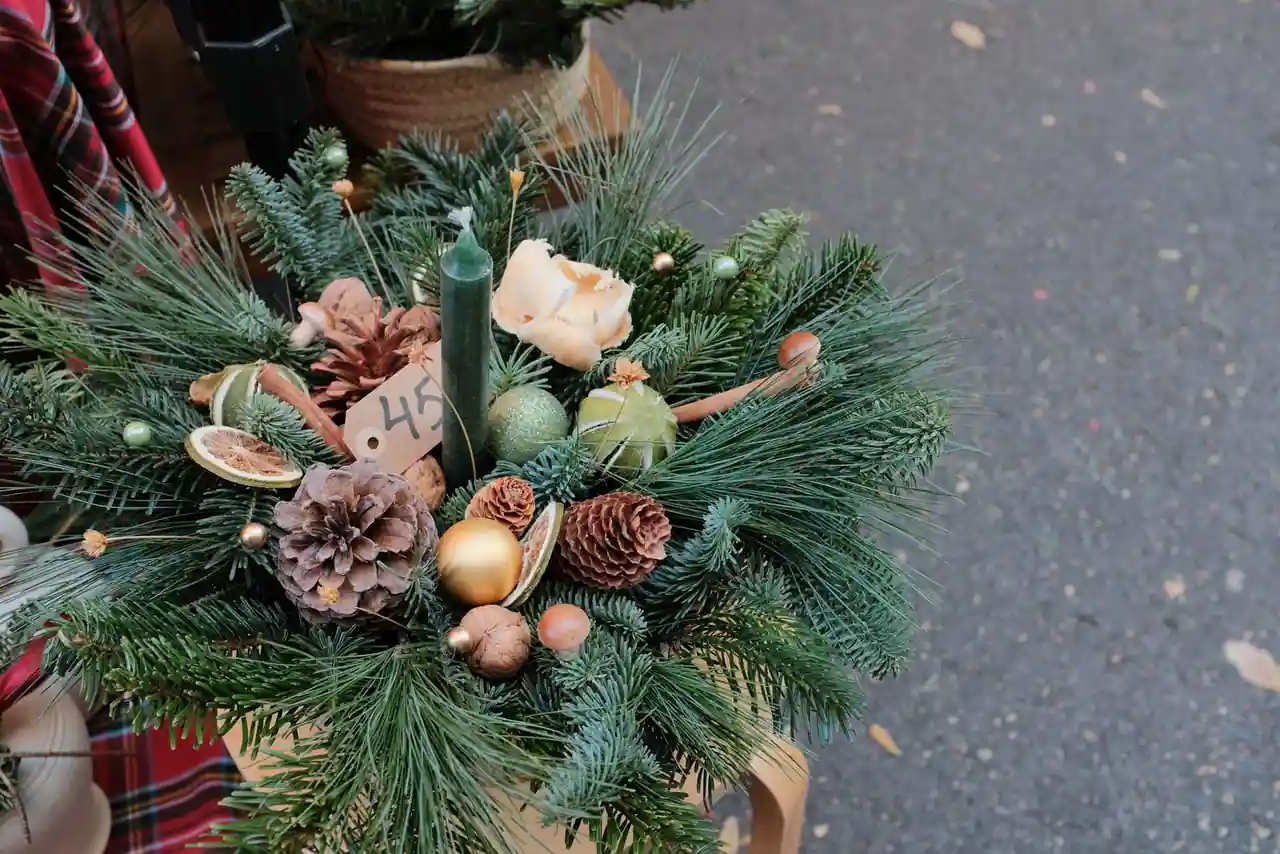 Composition de Noël aux tons naturels : branches de sapin, pommes de pin, orange séchée et bougie.
