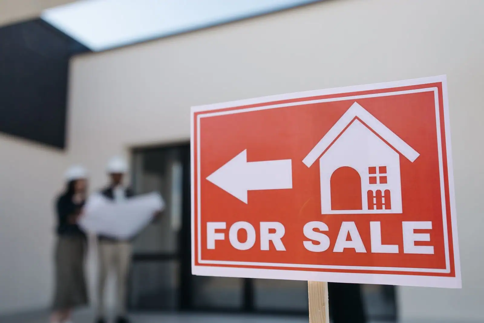 Panneau de mise en vente devant une maison moderne, un couple consultant des plans en arrière-plan