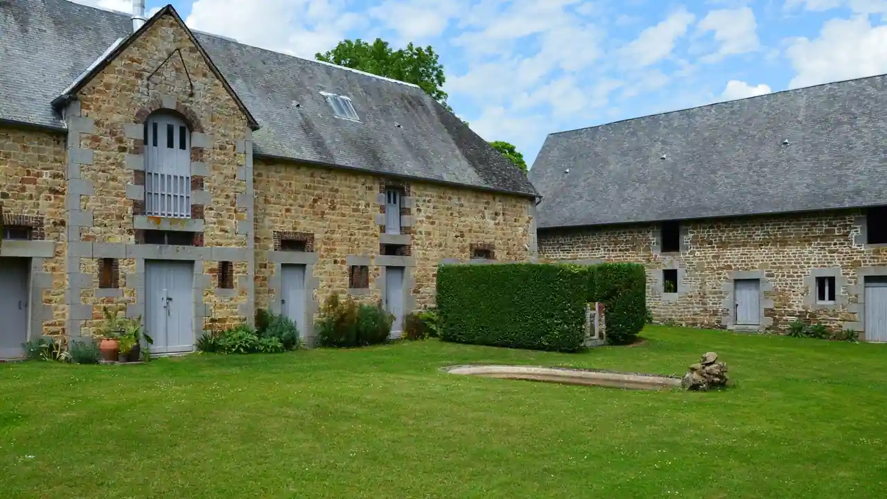 Corps de ferme normand en pierre, aux toitures d'ardoise, disposé autour d'une cour enherbée bordée de haies
