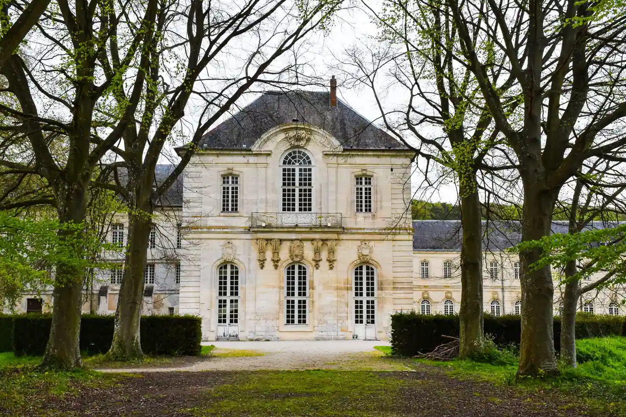 Demeure classique en pierre aperçue au bout d'une allée bordée d'arbres et de haies taillées