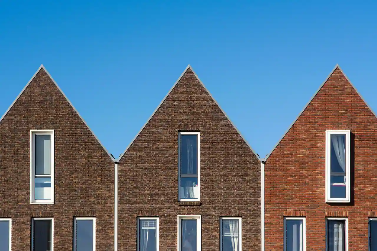 Façades en brique de trois maisons neuves à pignons triangulaires sous un ciel dégagé