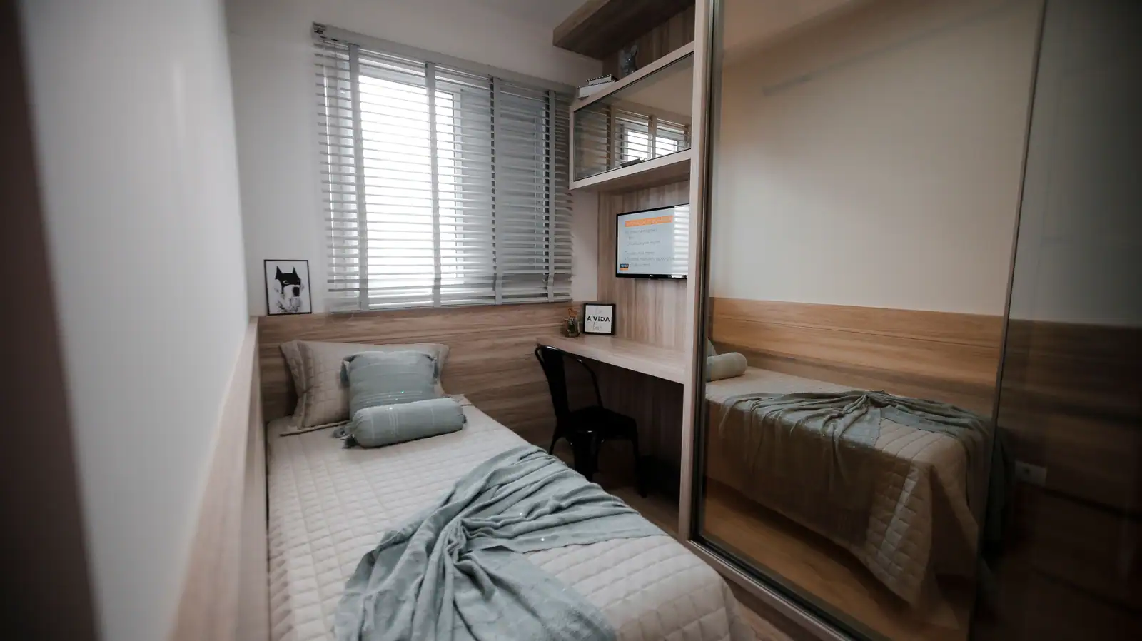Chambre étroite avec un lit simple dans la longueur, un placard à portes miroir et un bureau sous la fenêtre
