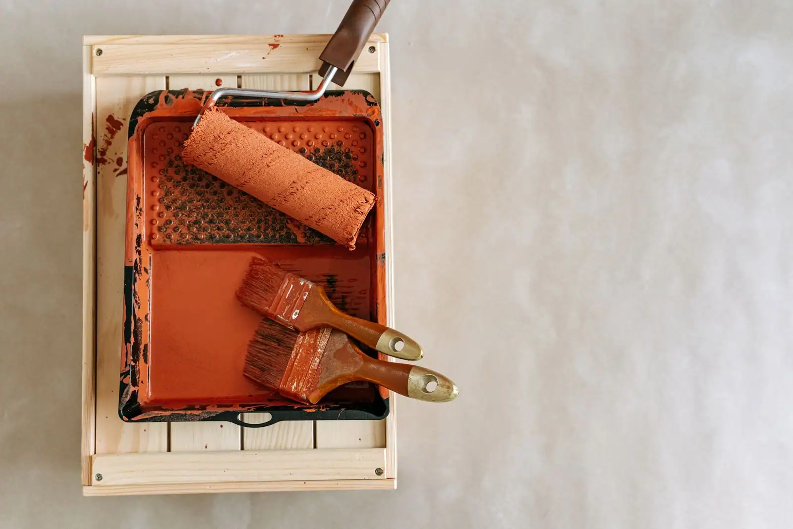 Bac à peinture terracotta avec rouleau et deux pinceaux, posé dans une caisse en bois clair