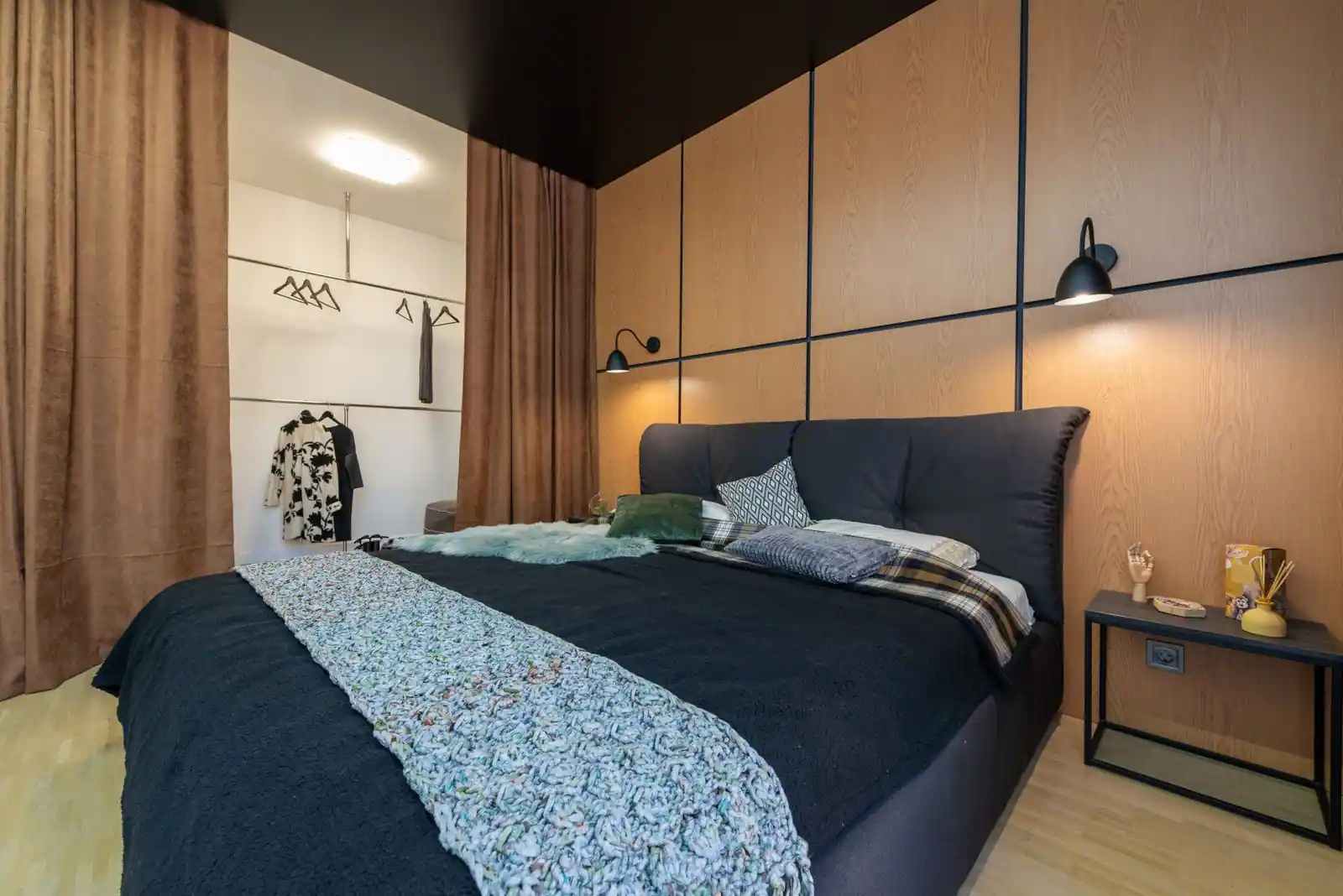 Chambre meublée d’un logement occupé : lit fait, table de chevet, mur d’armoires et penderie ouverte