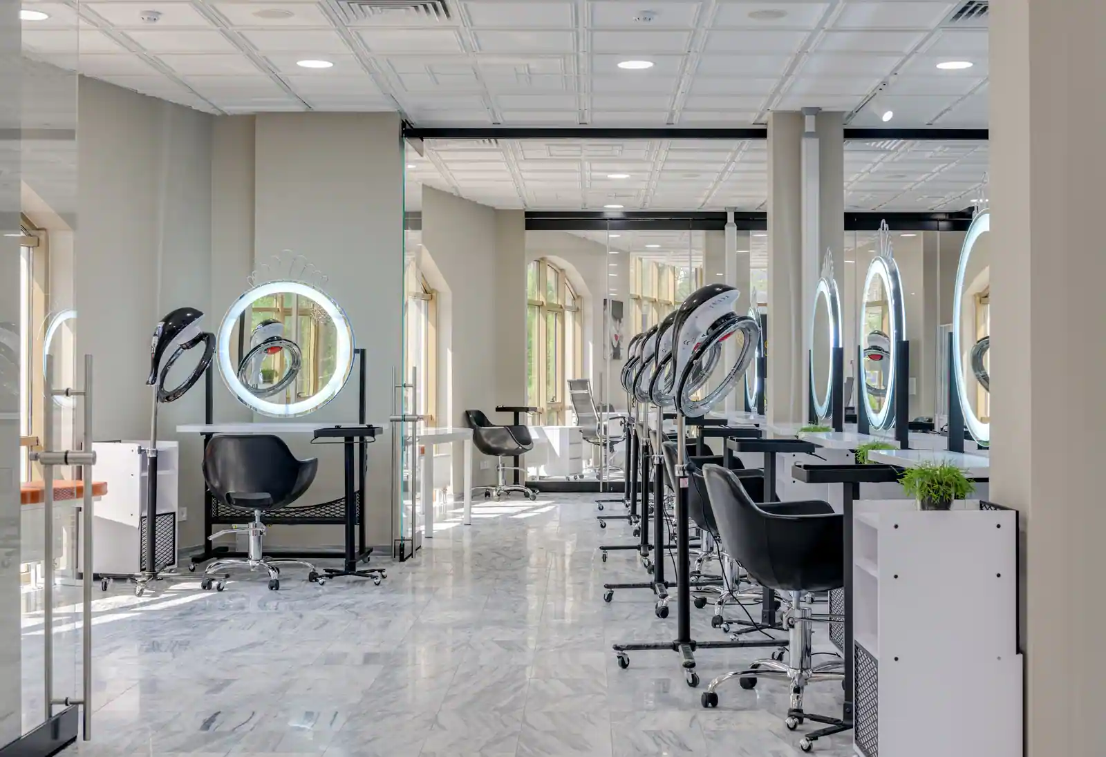 Intérieur d'un salon de coiffure moderne avec ses postes de coiffage, miroirs ronds éclairés et casques.