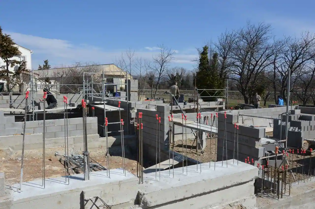 Chantier de maison individuelle au gros œuvre : murs en blocs de béton et armatures de chaînage en attente.