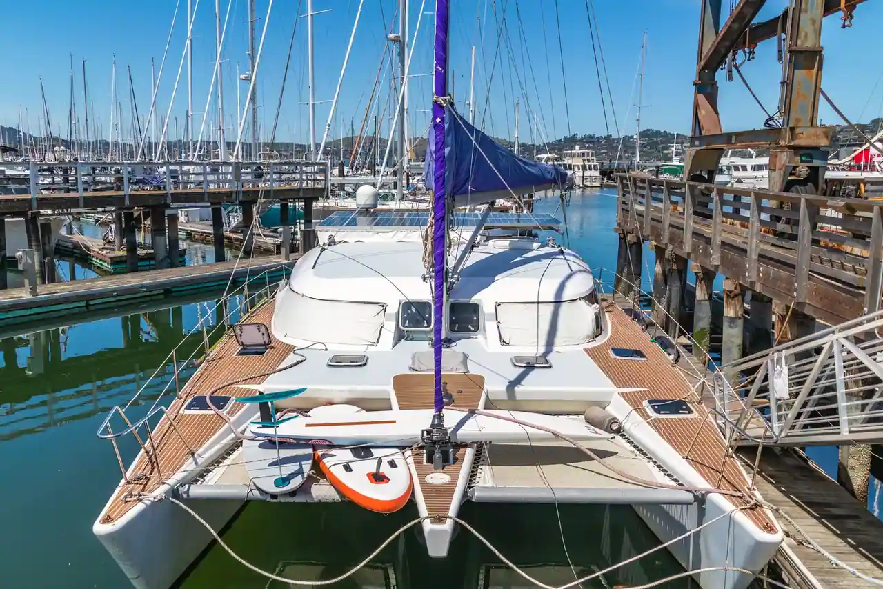 Catamaran de croisière blanc amarré le long d'un ponton, mât dressé et trampoline avant dégagé