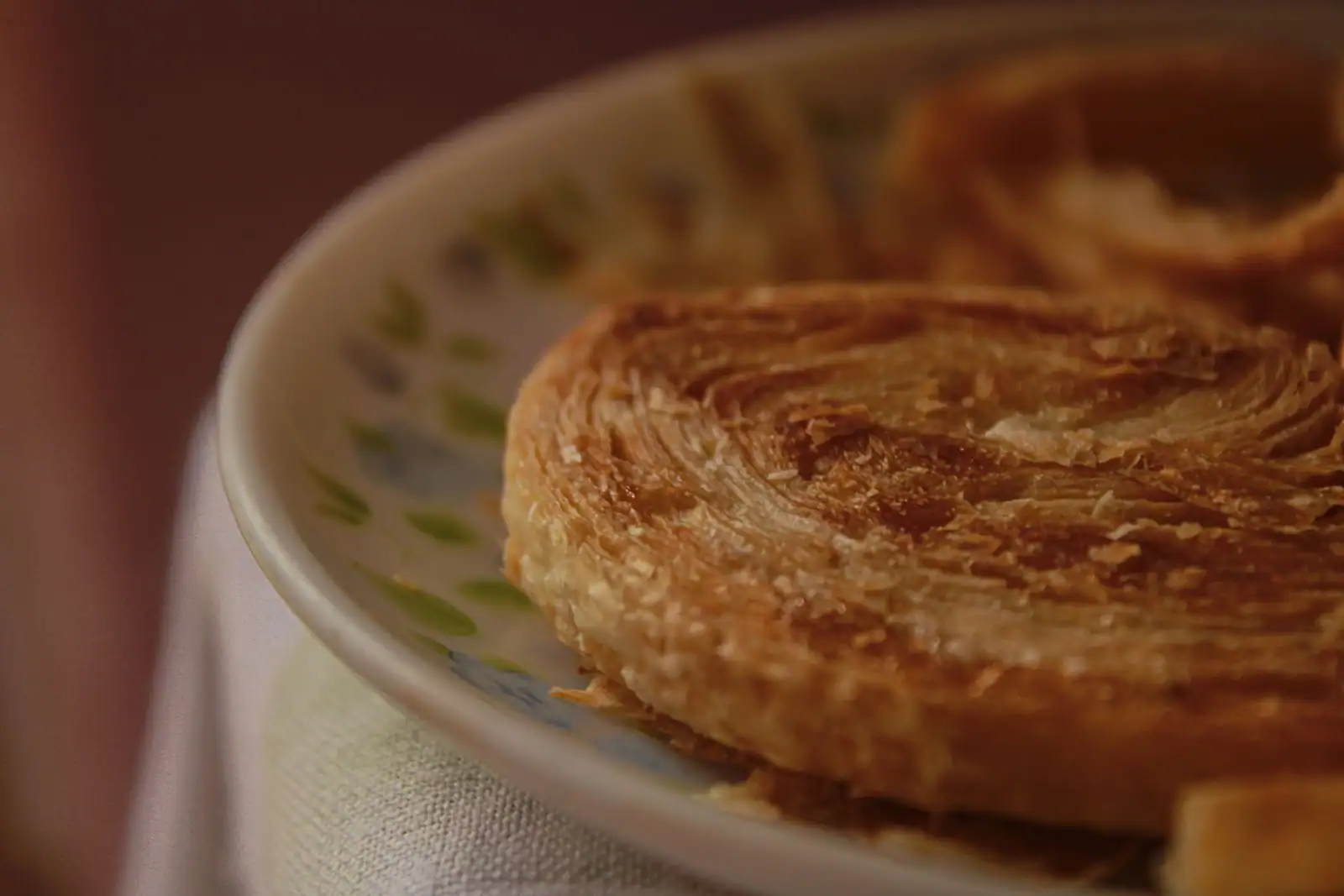Gâteau rond en pâte feuilletée dorée et caramélisée, posé sur une assiette à motifs verts, vu de près.