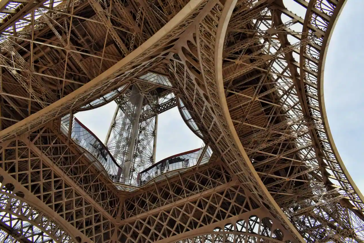 Vue en contre-plongée de la charpente en treillis de la tour Eiffel sous son premier étage