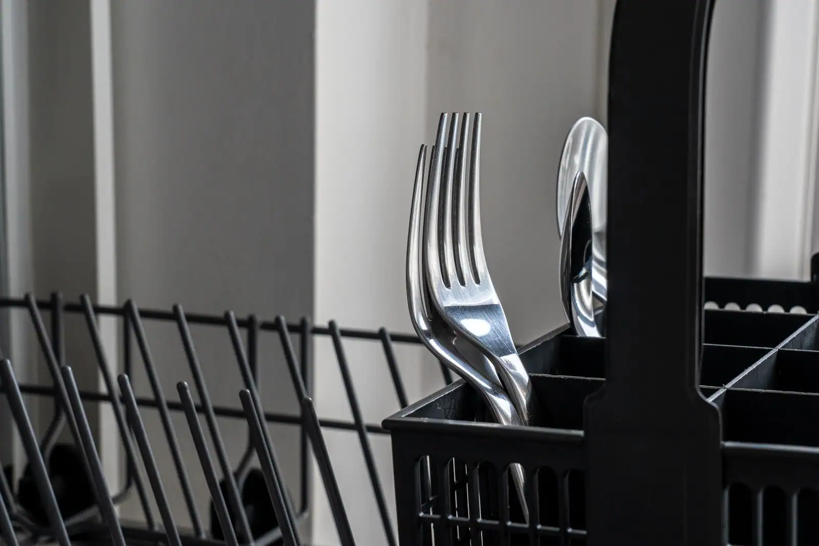 Gros plan sur le panier à couverts noir d'un lave-vaisselle, fourchettes et cuillère inox posées dedans.