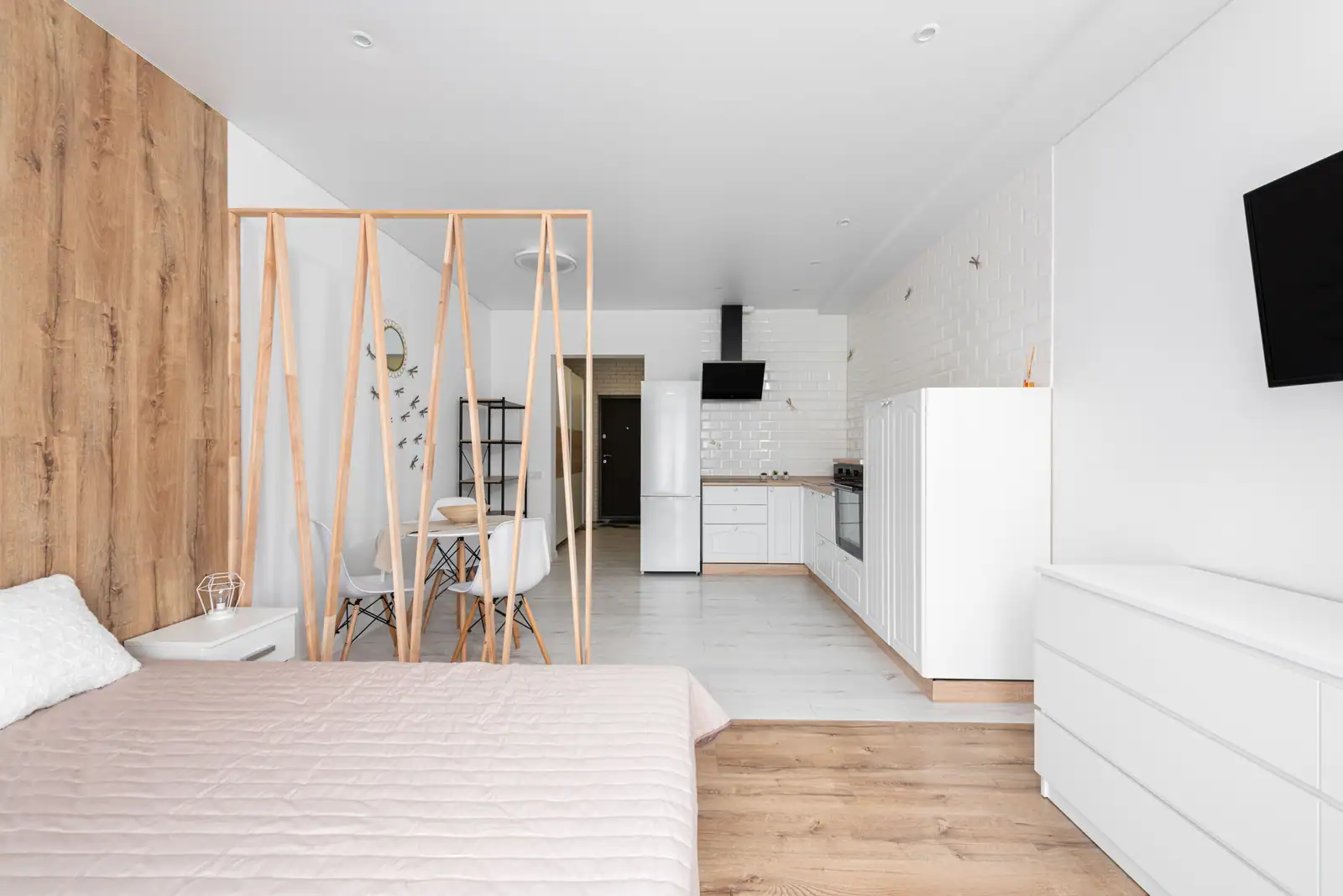 Pièce unique où le lit et la cuisine équipée se partagent le même volume, séparés par une claustra en bois.