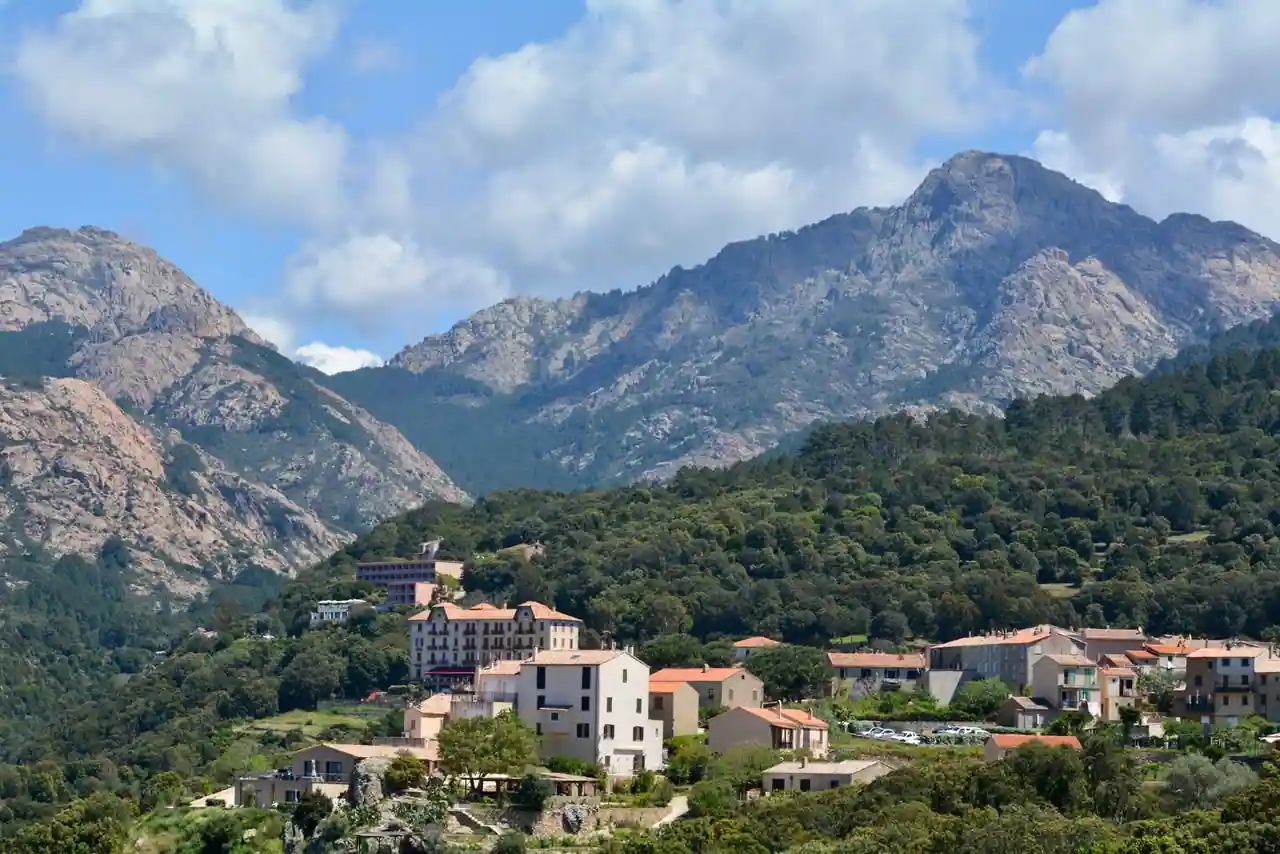 Village corse aux toits de tuiles adossé à la montagne, sommets granitiques en arrière-plan