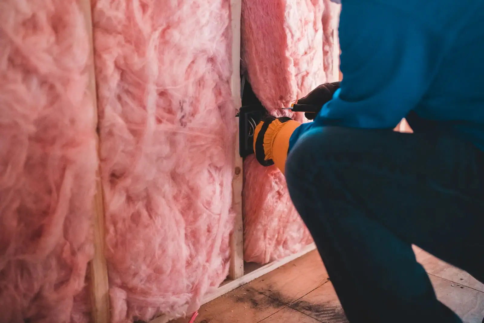 Pose de laine minérale rose entre les montants d'une paroi, sur un chantier d'isolation par l'intérieur
