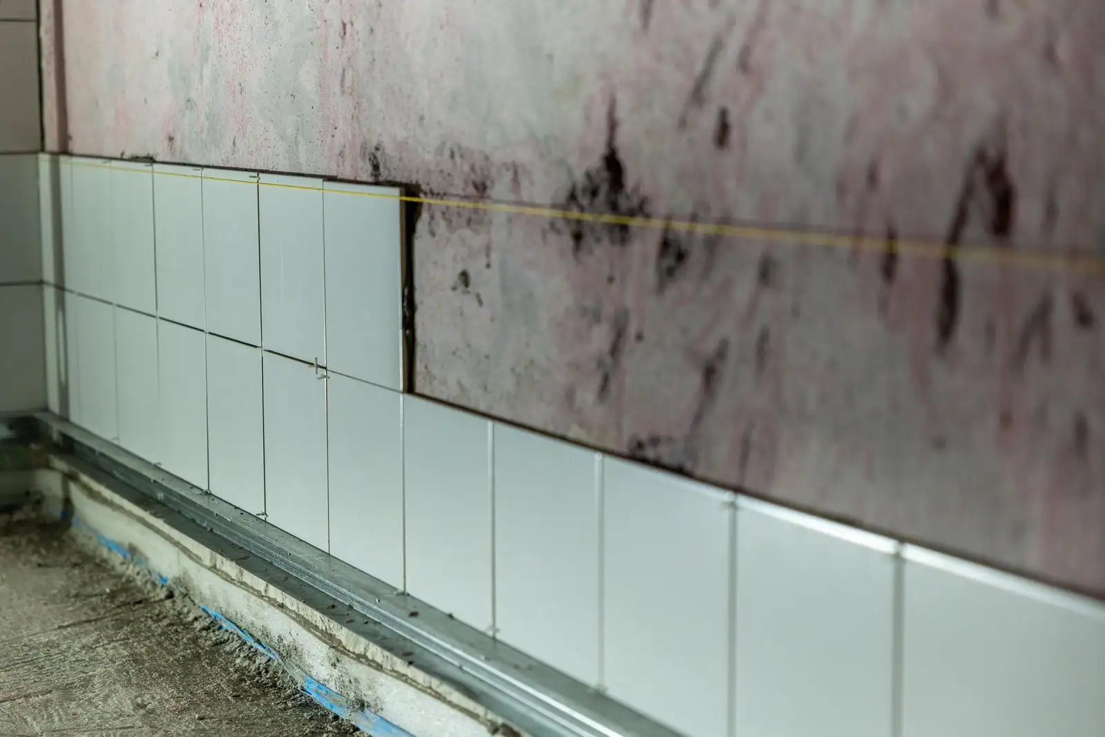 Carrelage mural blanc en cours de pose sur un mur préparé, avec rail de départ et cordeau tendu