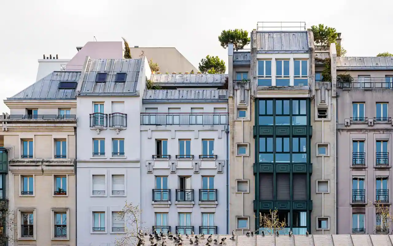 Façades d'immeubles parisiens mitoyens, balcons en ferronnerie et toitures de zinc sous un ciel clair.