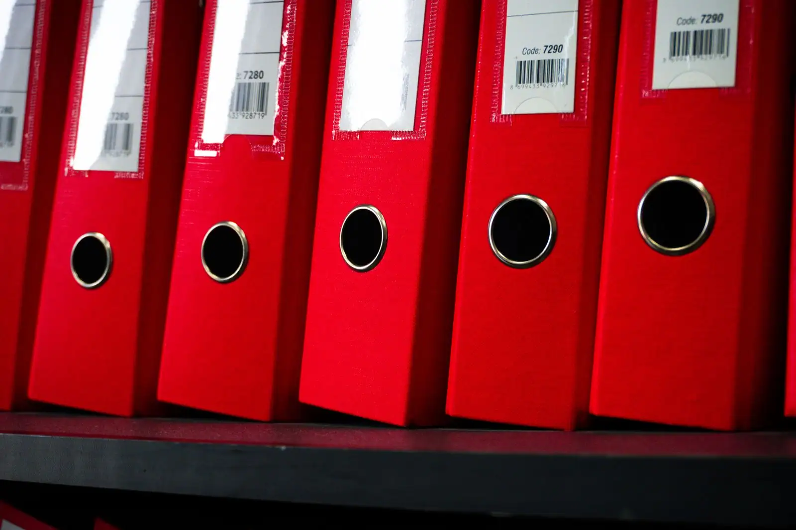 Classeurs d'archives alignés sur une étagère, étiquettes numérotées visibles sur chaque tranche.